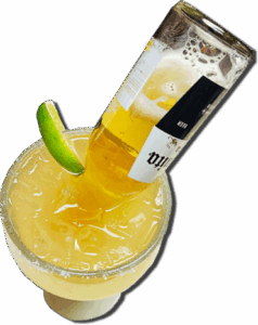 A margarita glass with a bottle of beer inserted, set against a vibrant backdrop of a Mexican restaurant.